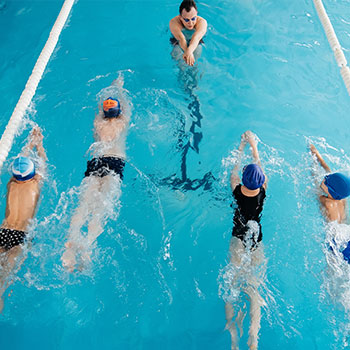 A young swimmer in a white cap and sunglasses is performing freestyle strokes in a clear swimming pool.