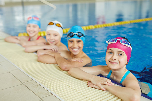 smiling young girl in a swimming pool wearing a blue swim cap and goggles, enjoying her time in the water